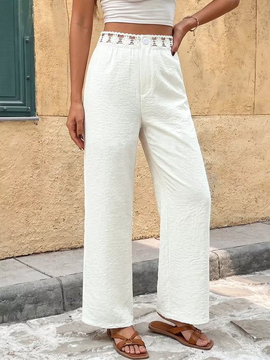Person wearing white textured pants and brown sandals standing against a beige wall.