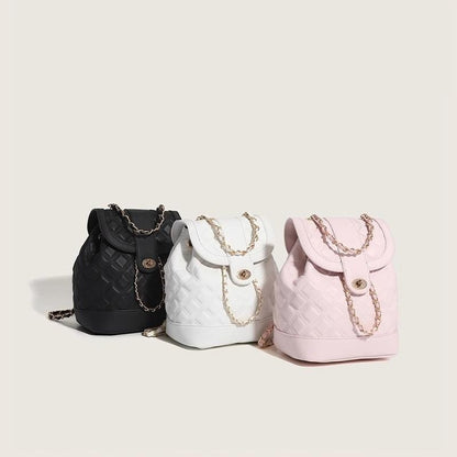 Three small backpacks in black, white, and pink with chain details on a beige background
