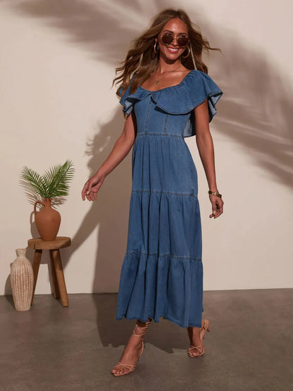 Woman wearing a blue dress standing in a room with a plant and vase.