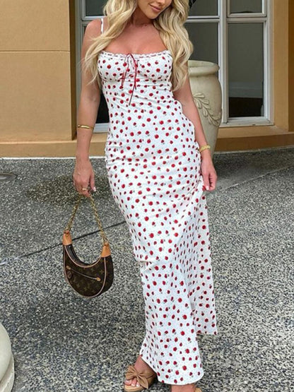 Woman in a white dress with red polka dots holding a handbag, standing on a pavement.