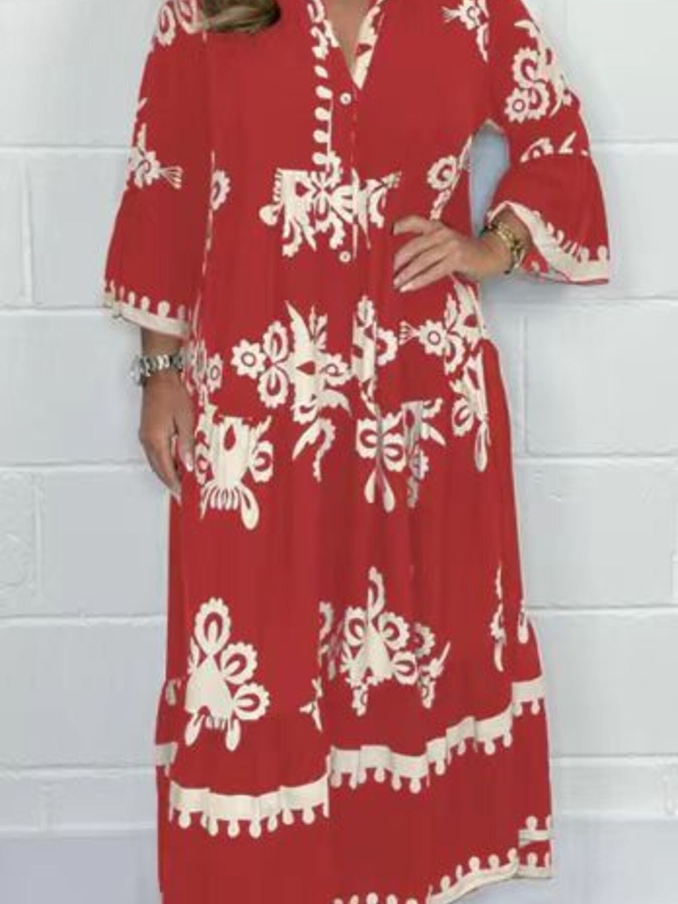 Red dress with white patterns worn by a person against a white brick wall.