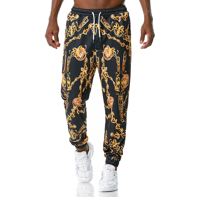 Black jogger pants with gold chain and lion head pattern worn by a person on a white background