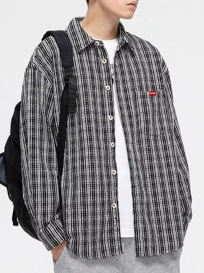 Person wearing a black and white checkered shirt with a small red logo, standing against a plain background.