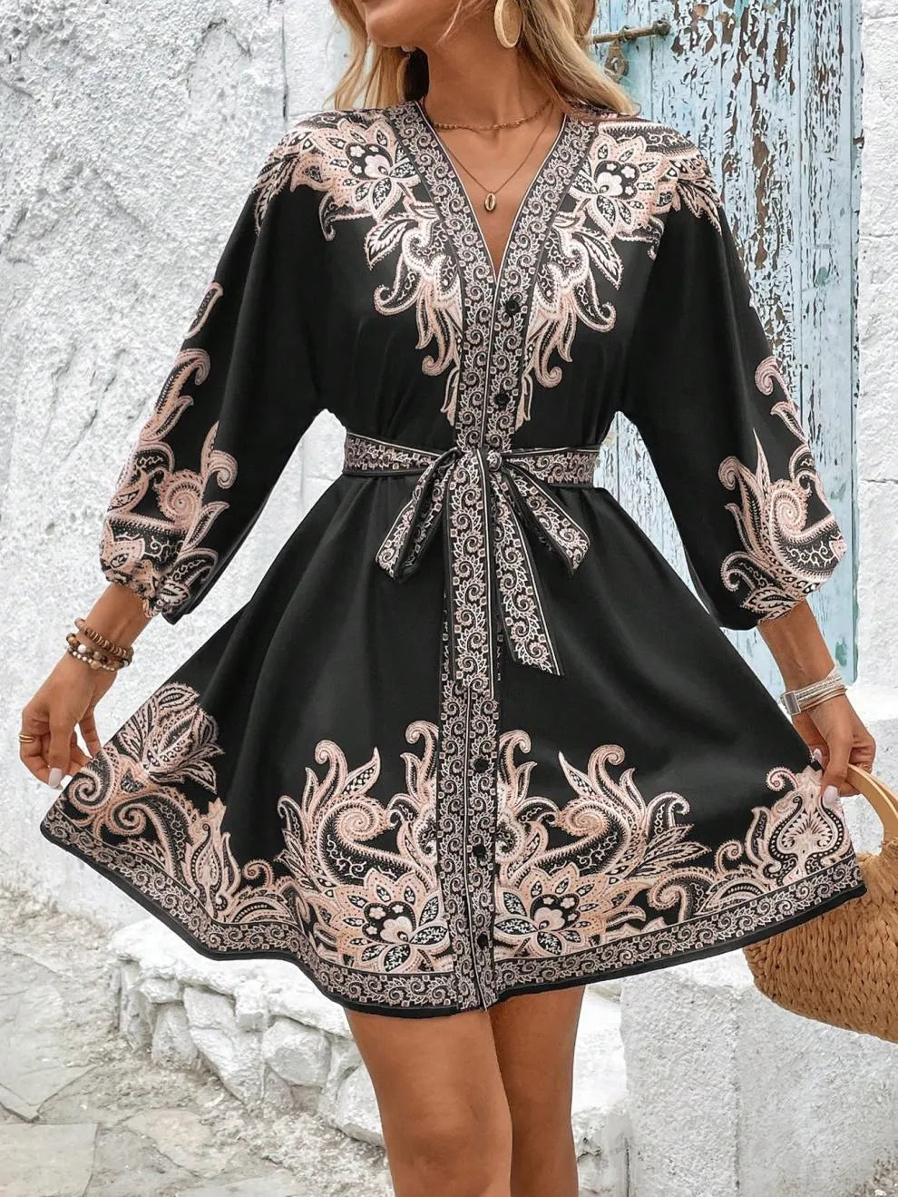 Black dress with intricate pink patterns worn by a person against a rustic wall.