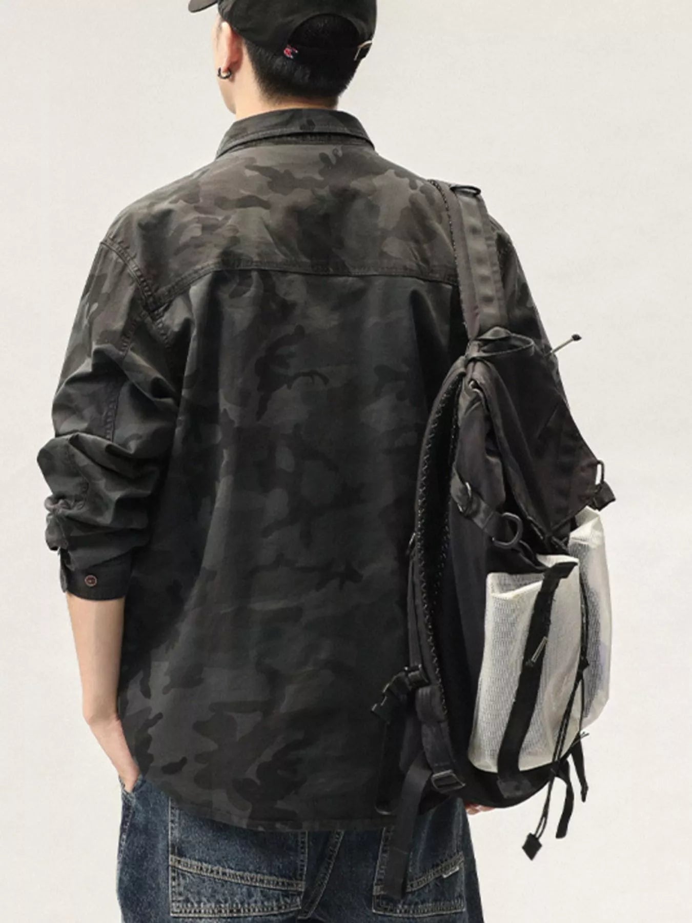 Person wearing a camouflage jacket and carrying a backpack with a white bag inside on a plain background
