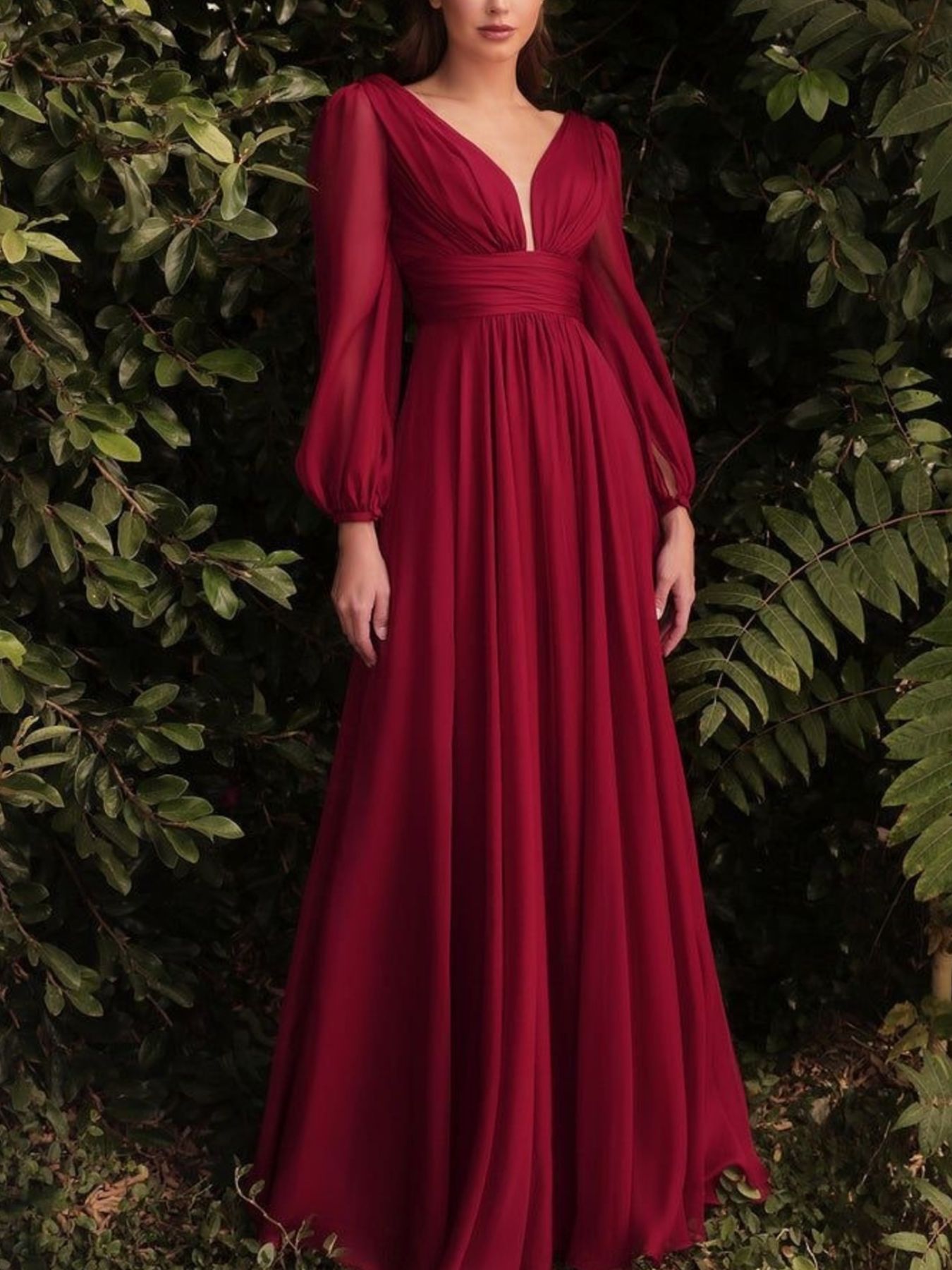 Red evening gown with long sleeves against a green leafy background