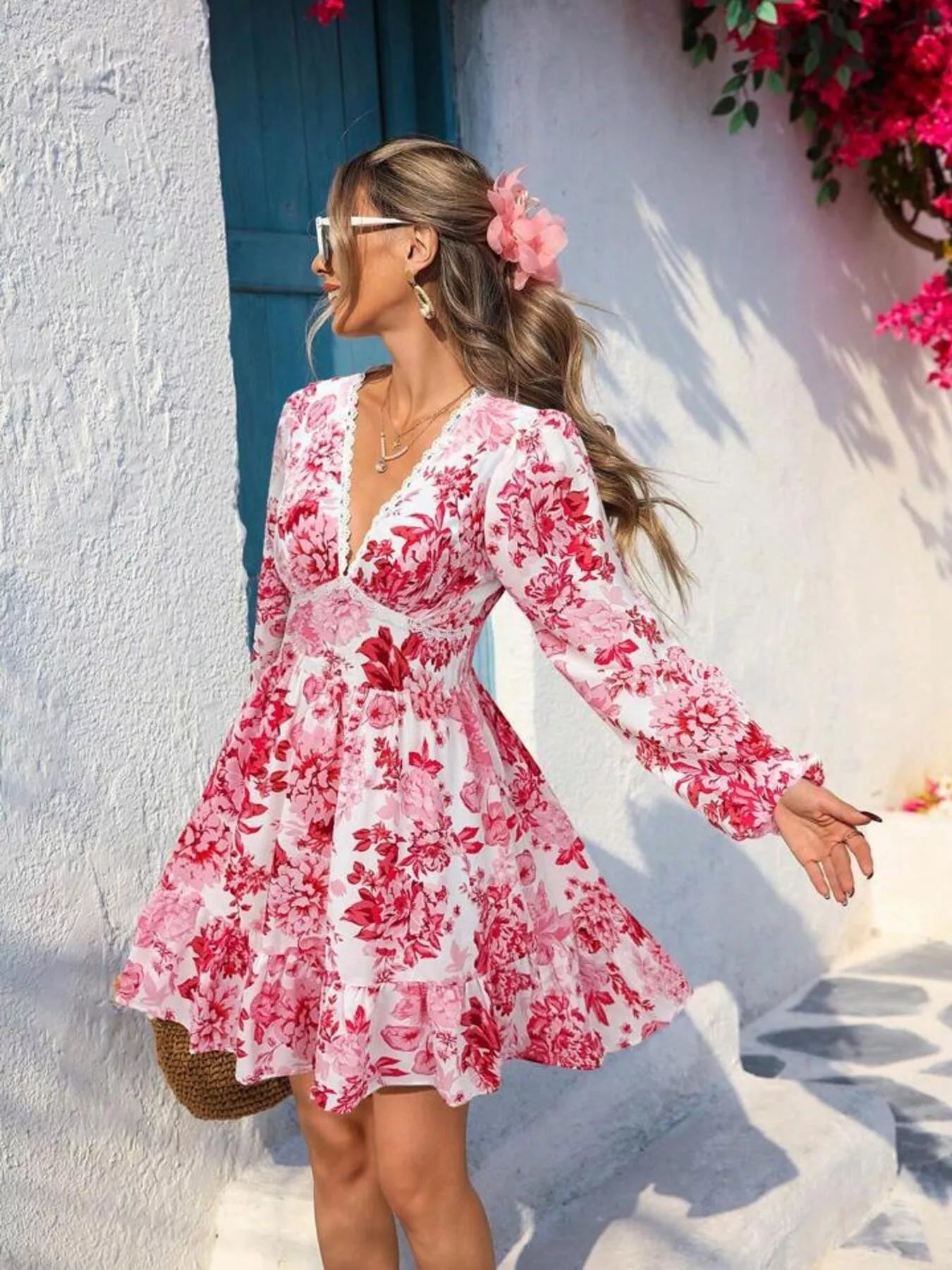 Woman wearing a pink floral dress standing in front of a white wall with a blue door.