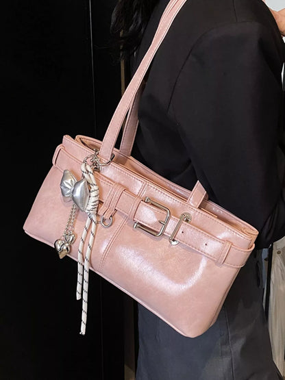 Pink handbag with decorative charms held by a person against a black background