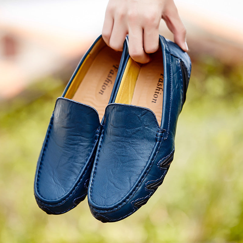 Blue loafers held by a hand with a blurred green background