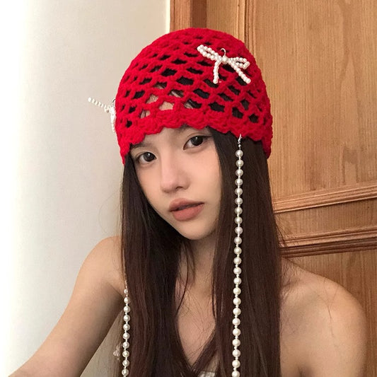 Person wearing a red knitted hat with pearl accents against a wooden background