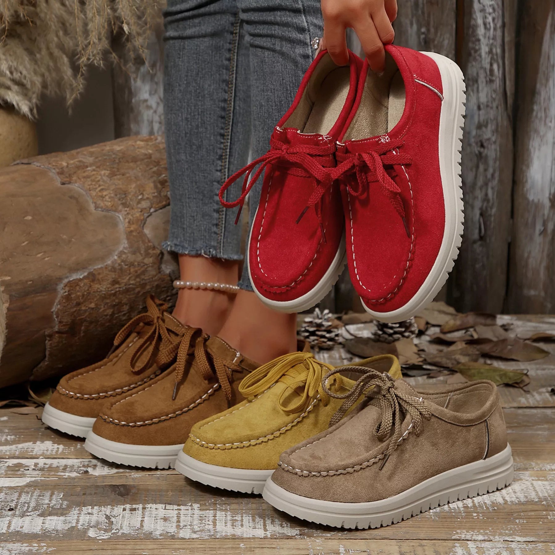 Red shoes held above a collection of brown, yellow, and red shoes on a wooden surface.