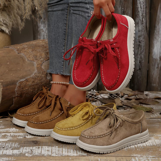 Red shoes held above a collection of brown, yellow, and red shoes on a wooden surface.