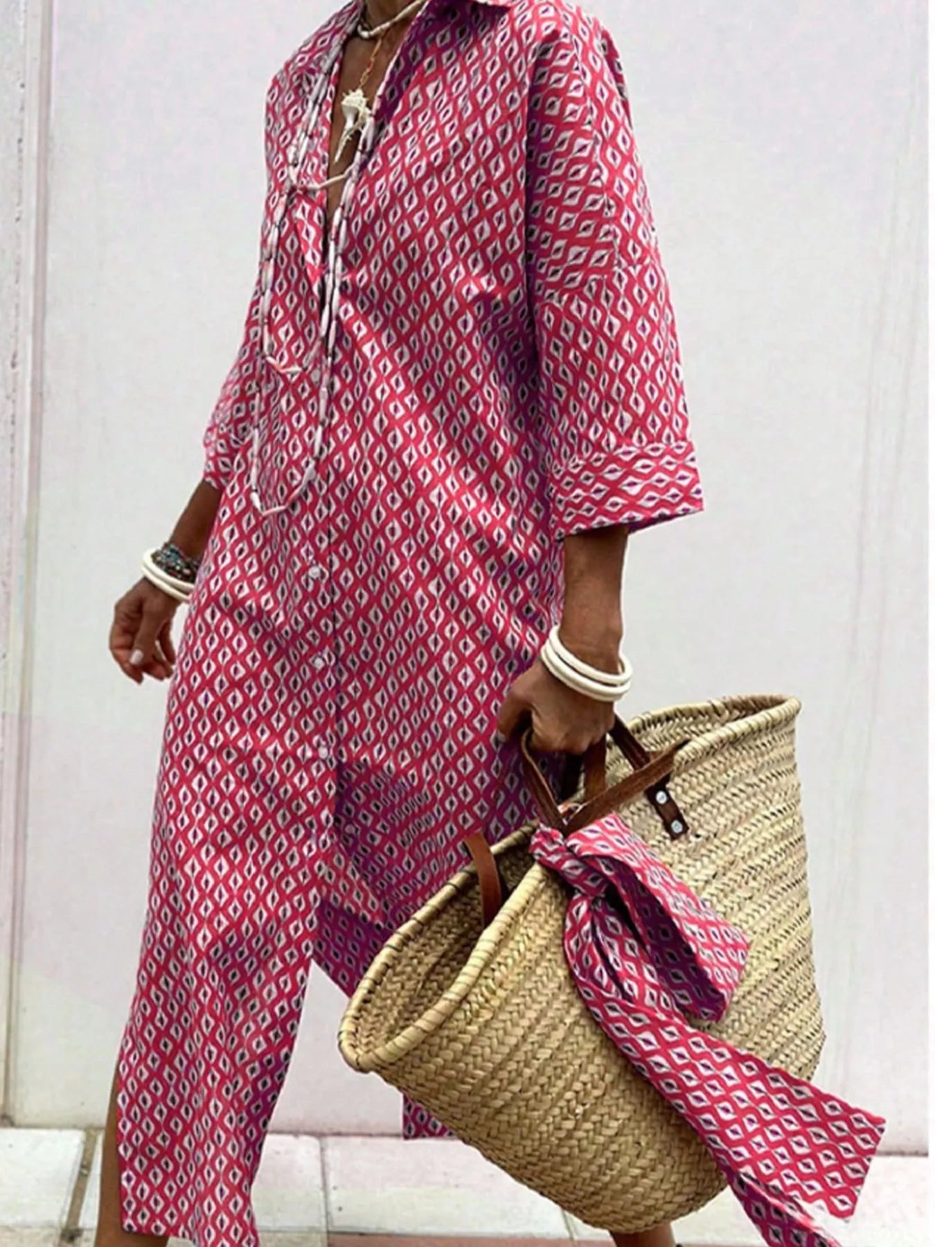 Person wearing a pink patterned dress holding a straw bag against a white background