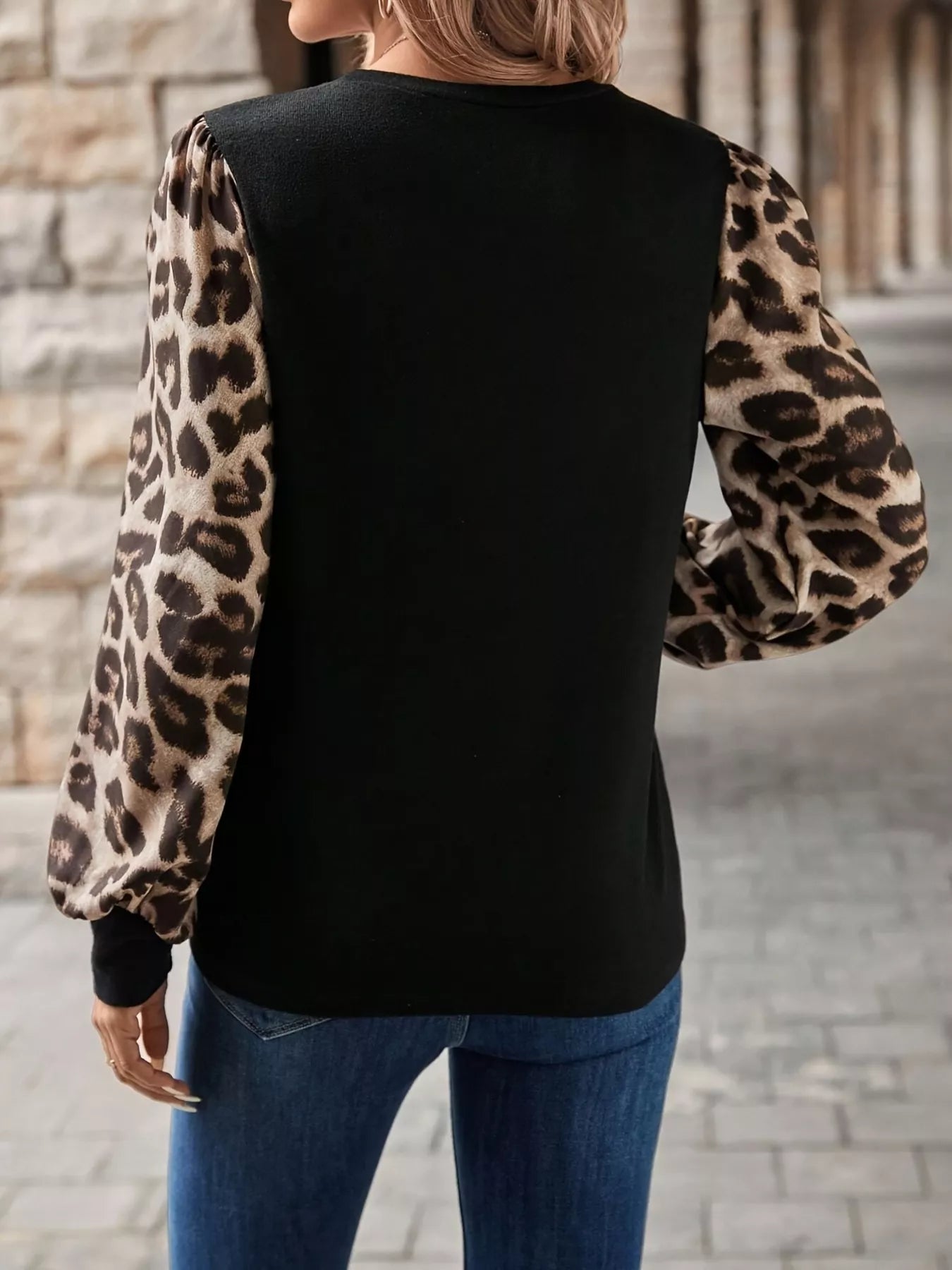 Person wearing a black top with leopard print sleeves in an urban setting