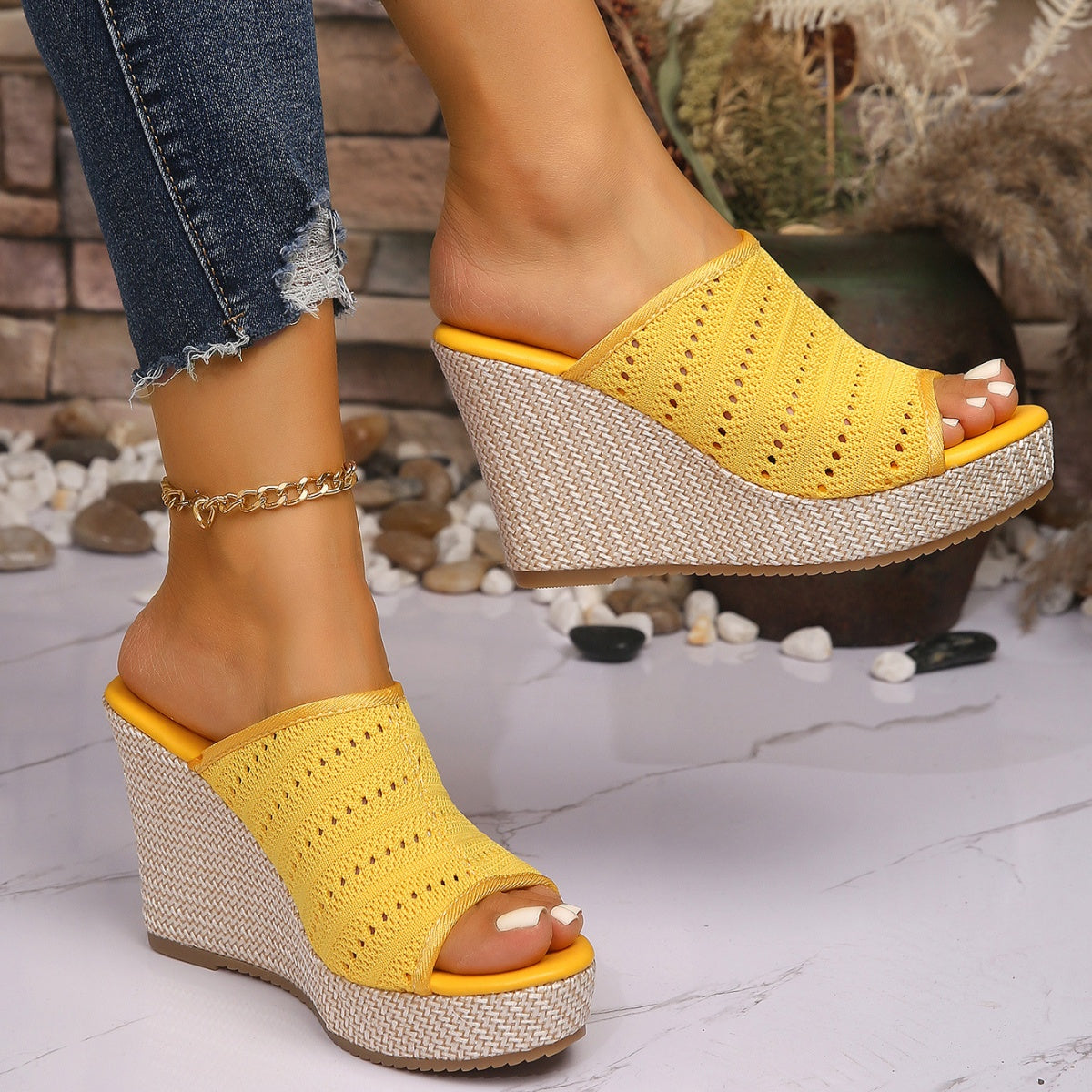 Yellow wedge sandals worn with denim jeans on a light stone floor.