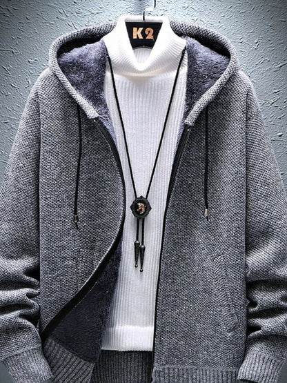 Gray hooded jacket over a white turtleneck sweater with a dark bolo tie on a textured gray background.
