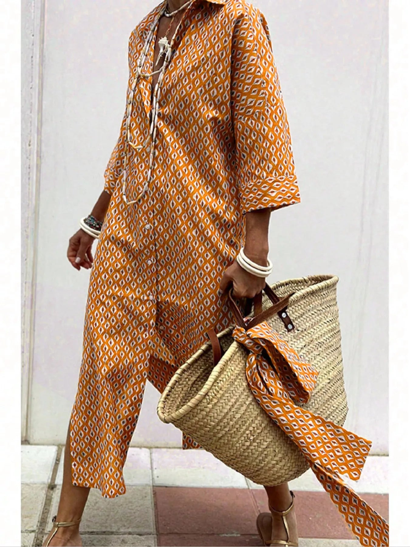 Person wearing an orange patterned dress holding a straw bag on a light background