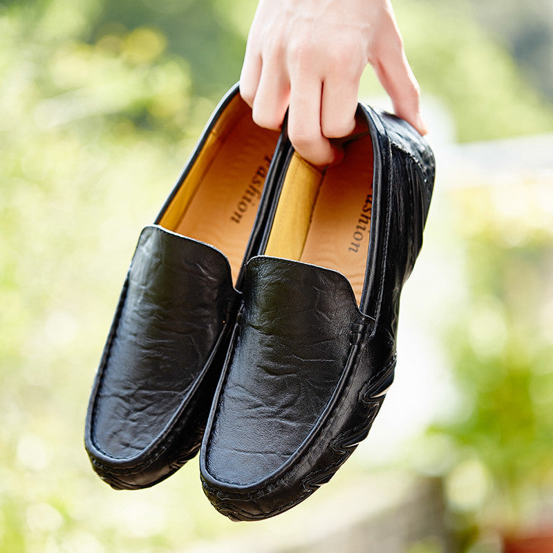 Black leather loafers held by a hand with a blurred green background