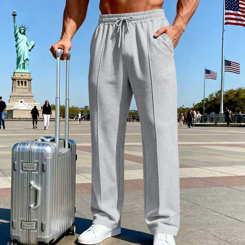 Person wearing gray sweatpants holding a silver suitcase with the Statue of Liberty and American flags in the background.