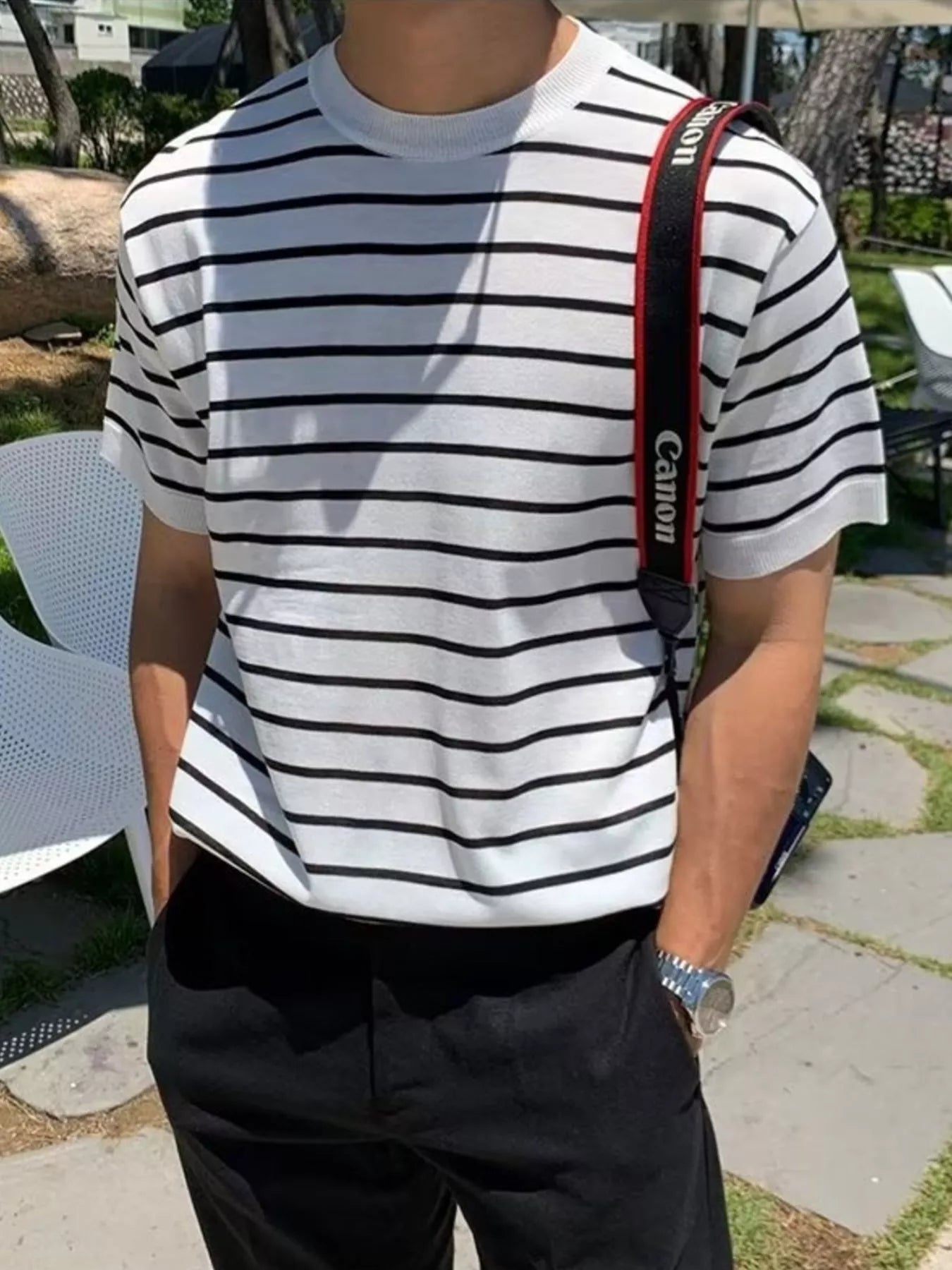 Person wearing a white and black striped shirt with a Canon camera strap over shoulder outdoors.