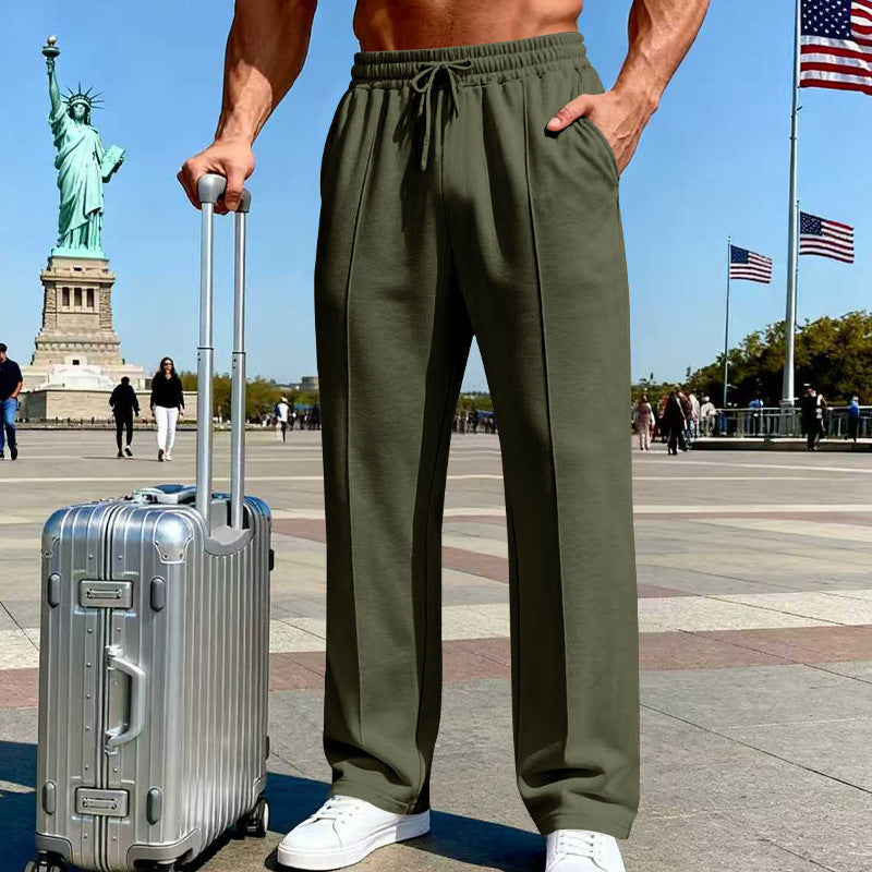 Person wearing green pants with a silver suitcase in front of the Statue of Liberty and American flags.