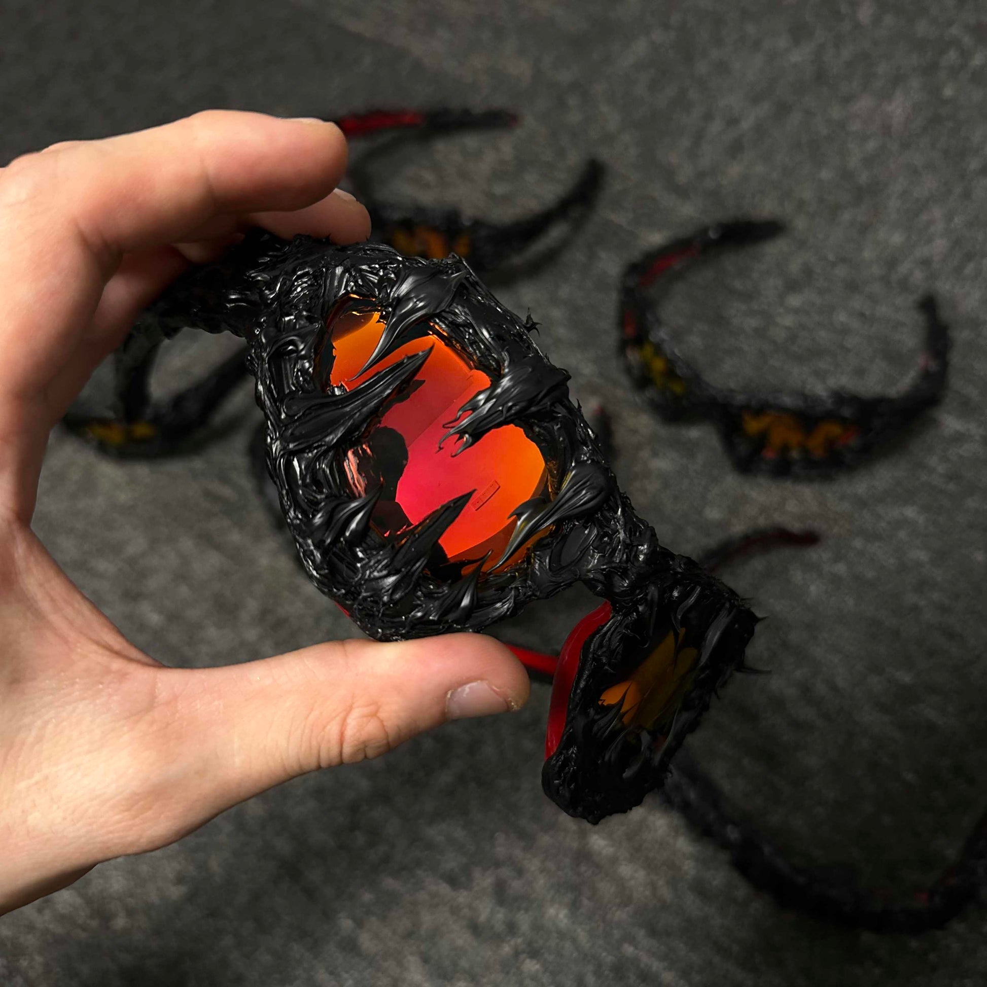 Hand holding a black and orange dragon-shaped object on a dark surface