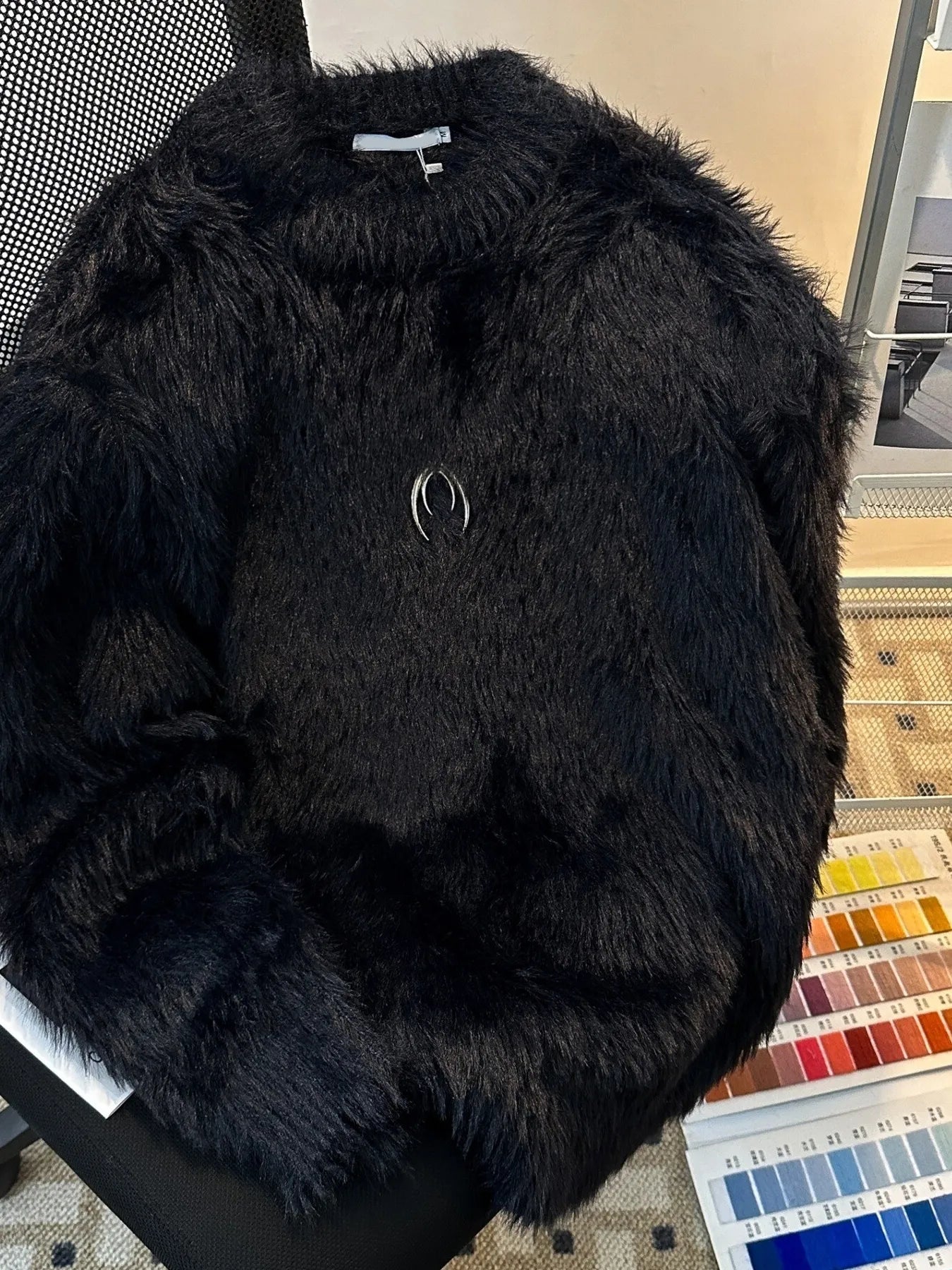 Black fluffy jacket on a chair with a color swatch in the background