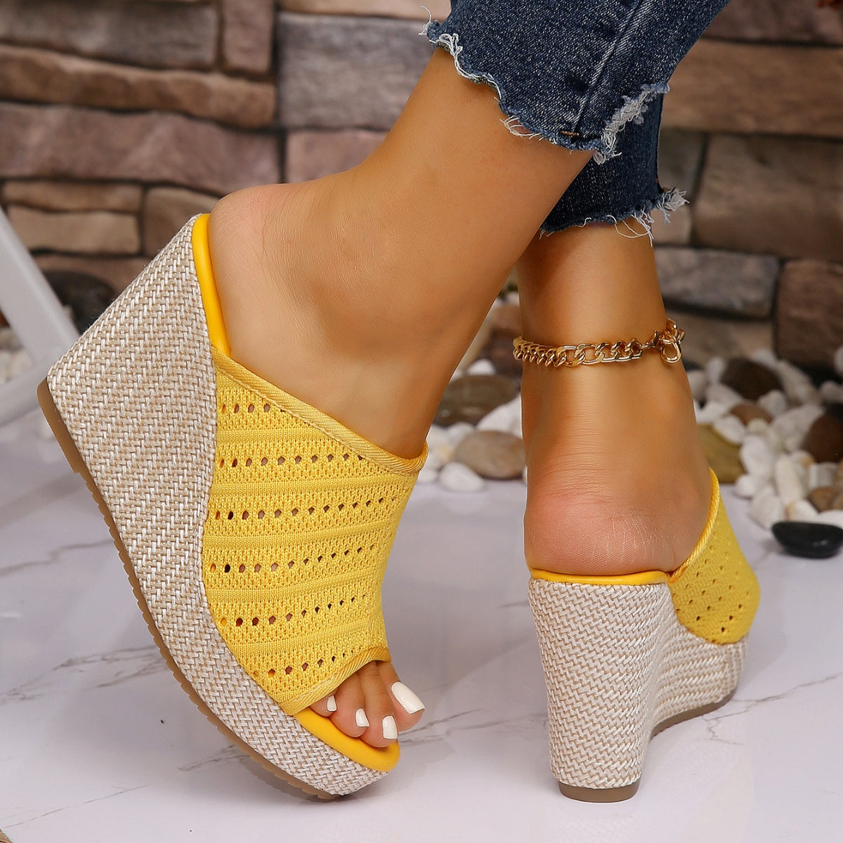 Yellow wedge sandals with woven design on a stone and pebble background