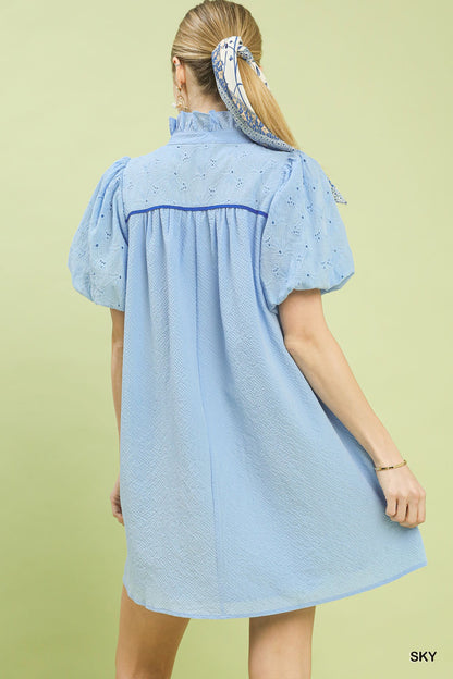 Woman wearing a light blue dress with embroidered details on a green background