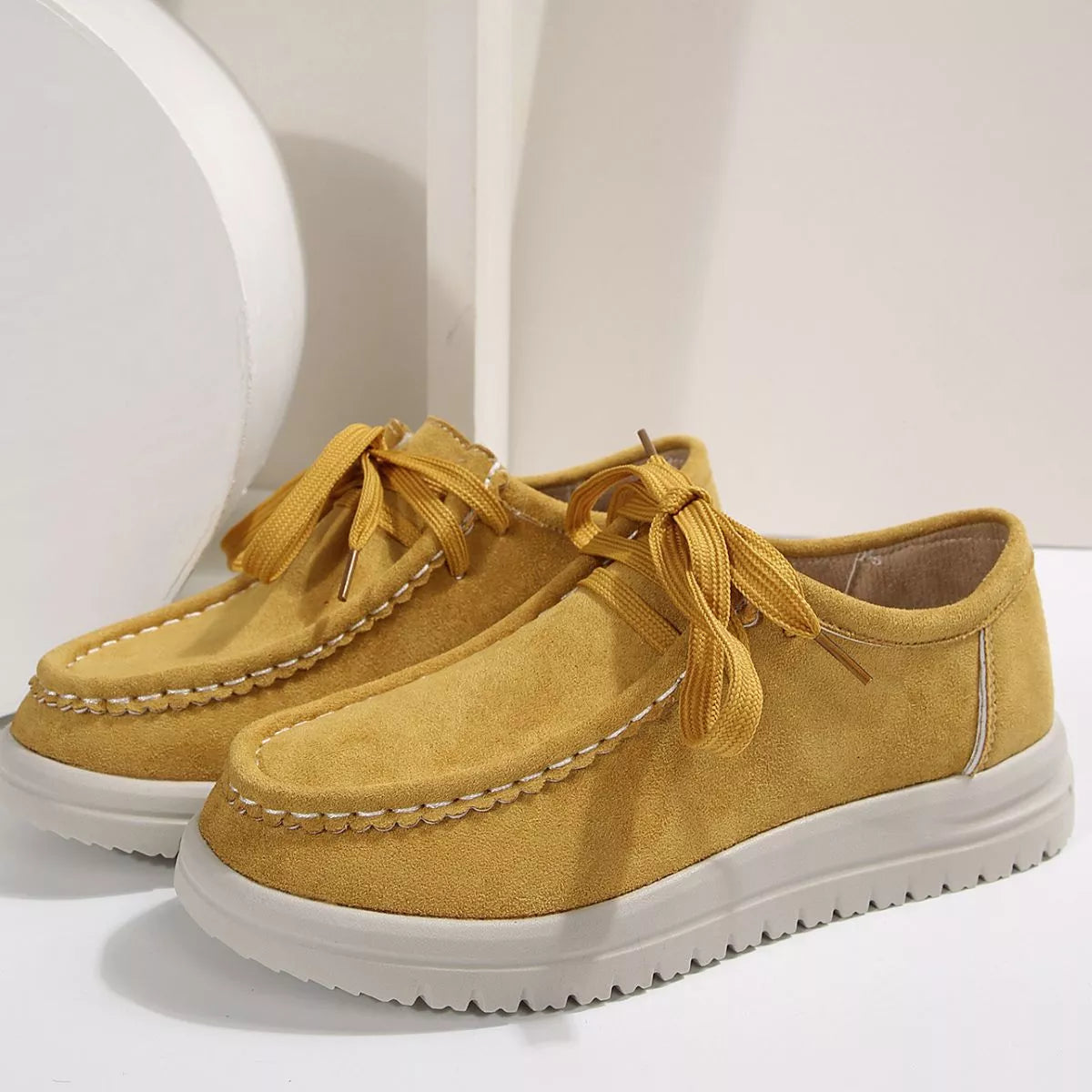 Pair of yellow suede shoes with white soles on a light background