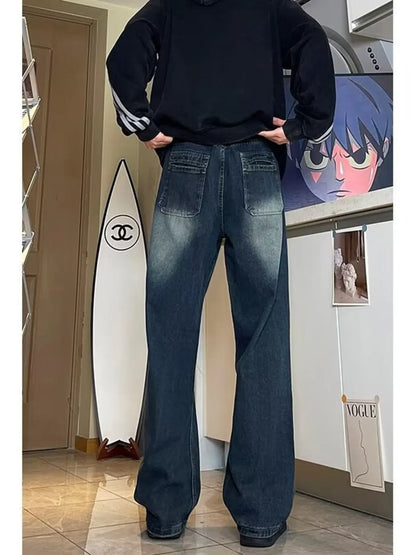 Person wearing a black hoodie and blue jeans standing in a room with a white wall and door.