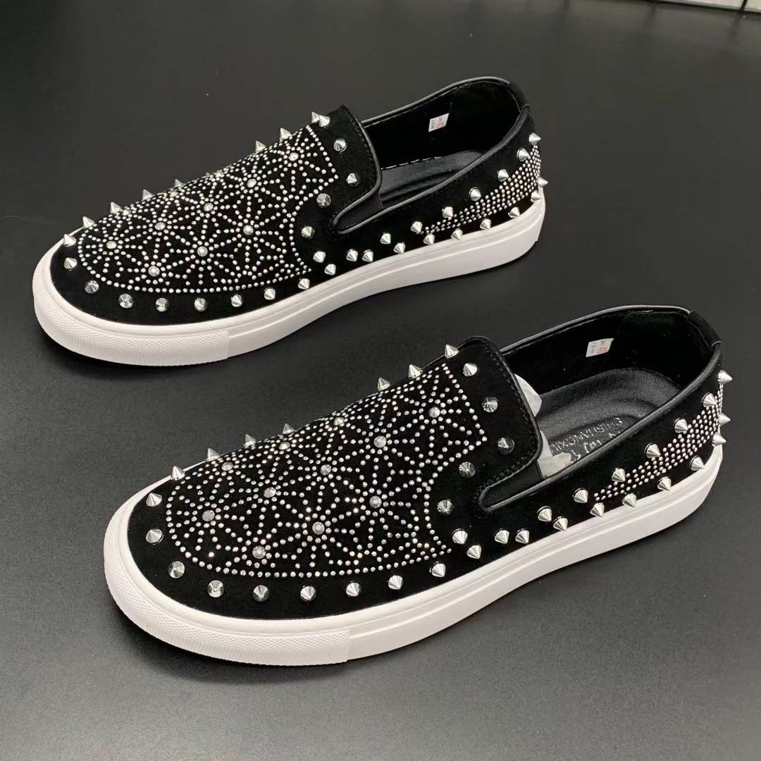 Black slip-on shoes with white soles and rhinestone embellishments on a gray surface
