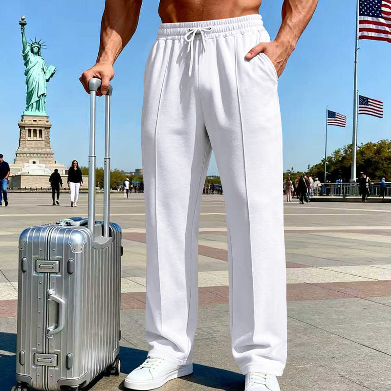 Person wearing white pants standing next to a silver suitcase with the Statue of Liberty and American flags in the background.