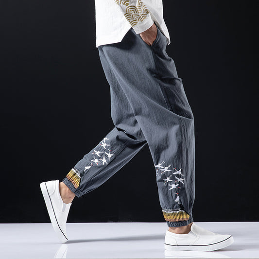 Person wearing gray jogger pants with white floral patterns and white sneakers on a black background