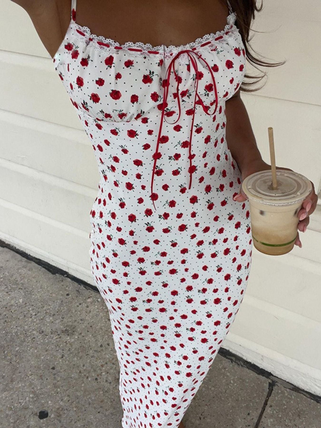 Person wearing a red and white floral dress holding a drink.