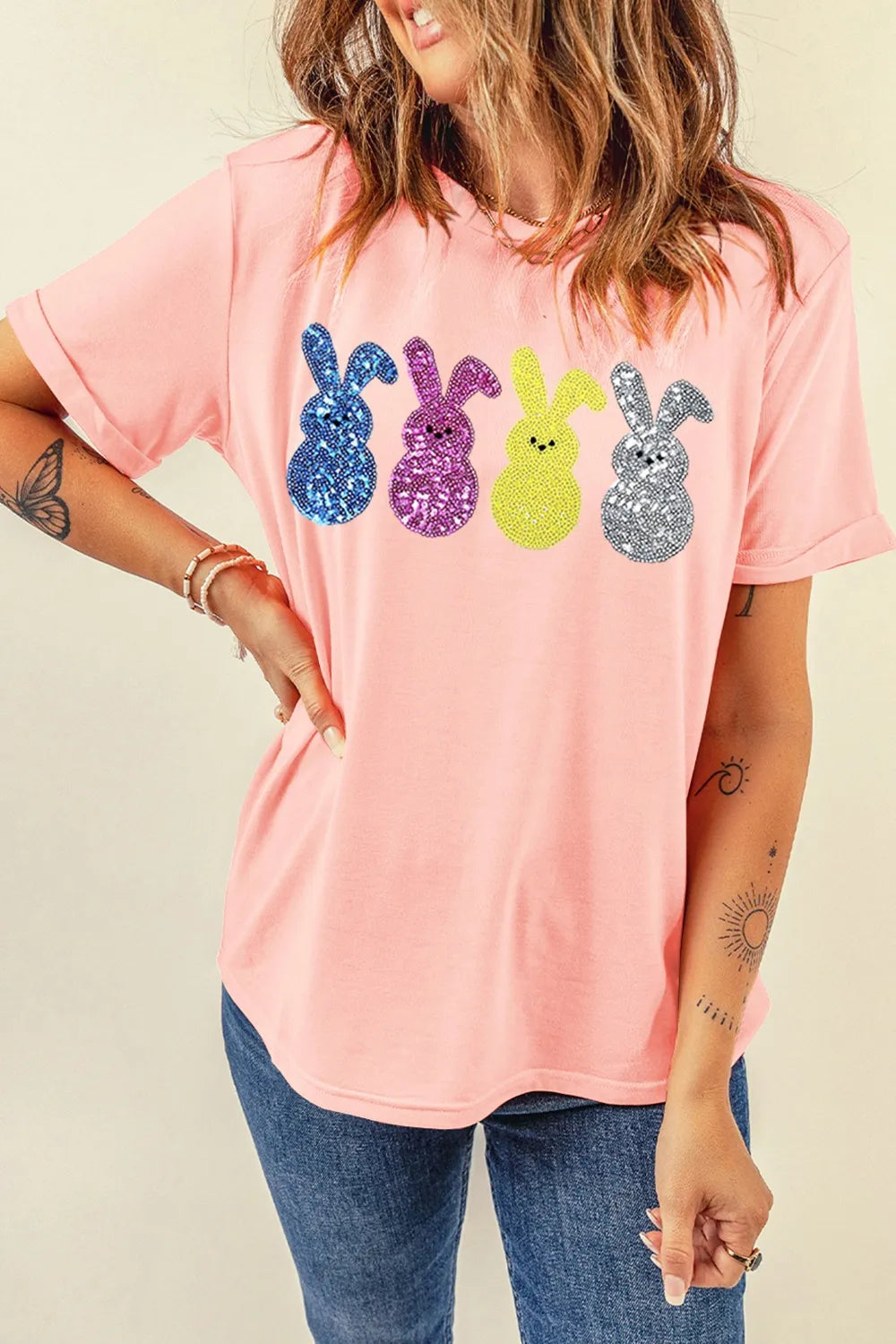 Person wearing a pink t-shirt with colorful sequin bunny designs on a beige background