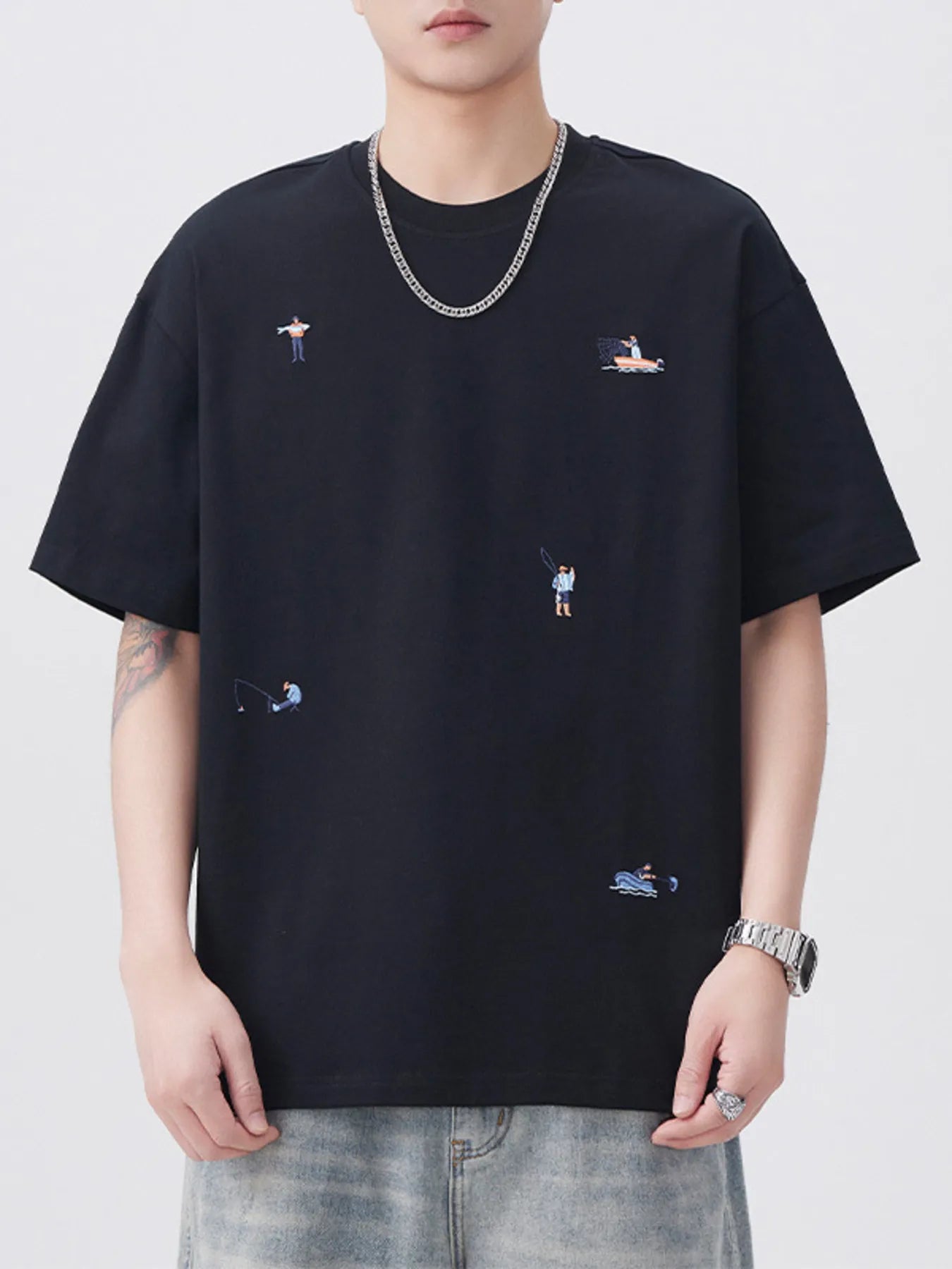 Person wearing a black t-shirt with small embroidered designs on a plain background