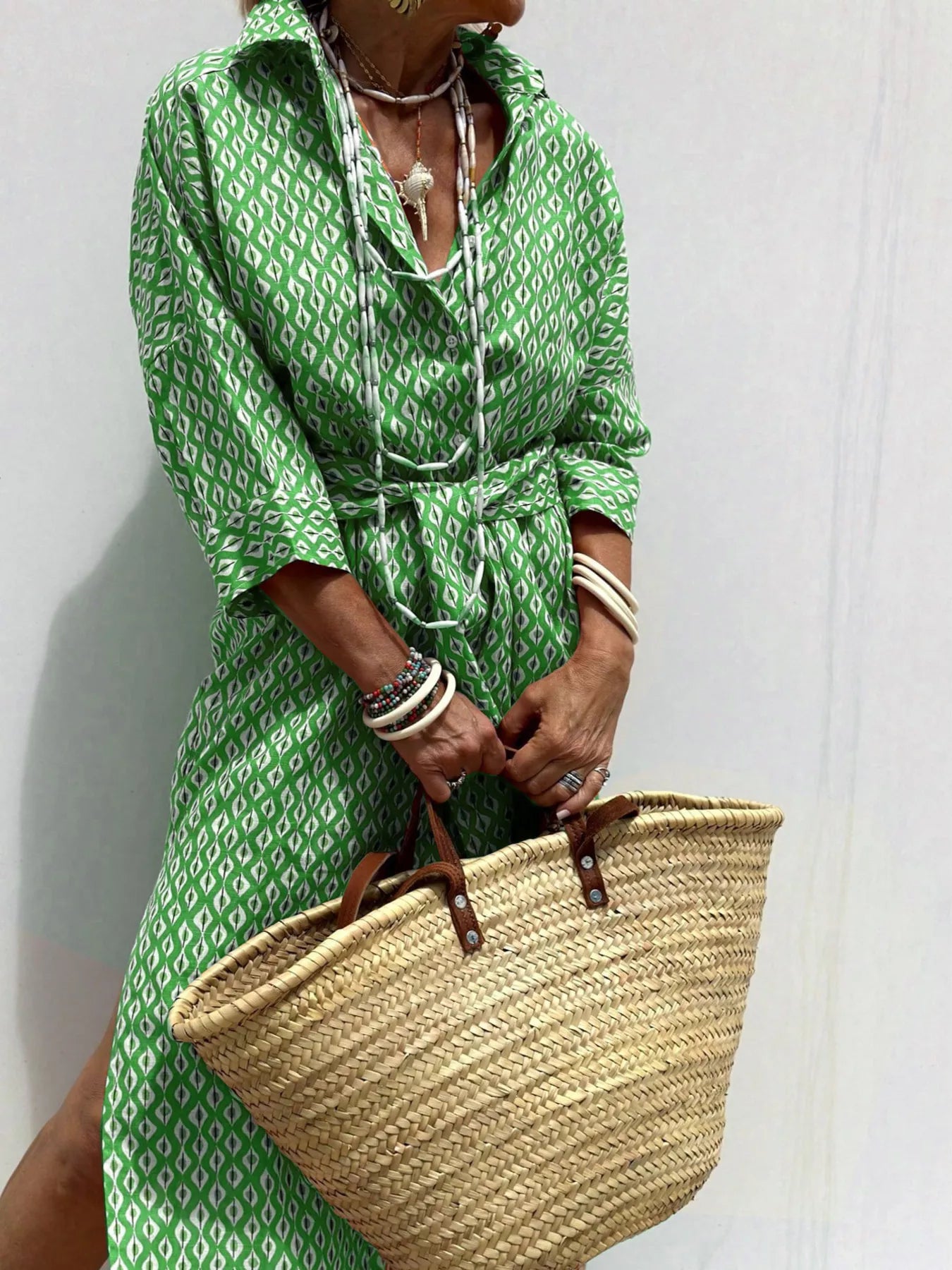 Person wearing a green patterned dress holding a straw bag against a white background