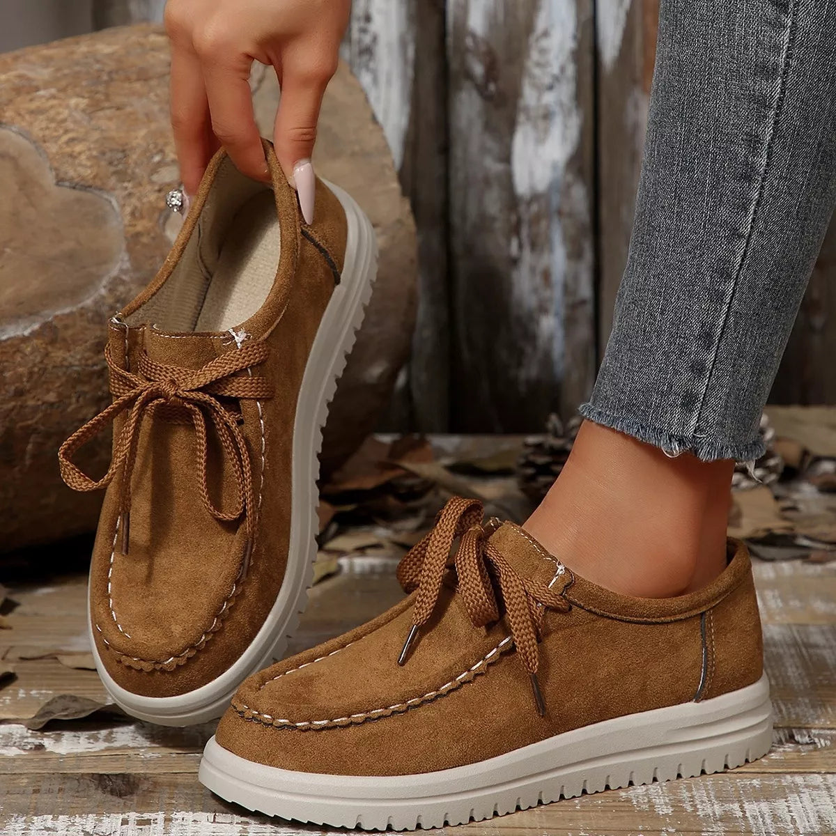 Brown suede shoes with white soles worn by a person on a rustic wooden floor.