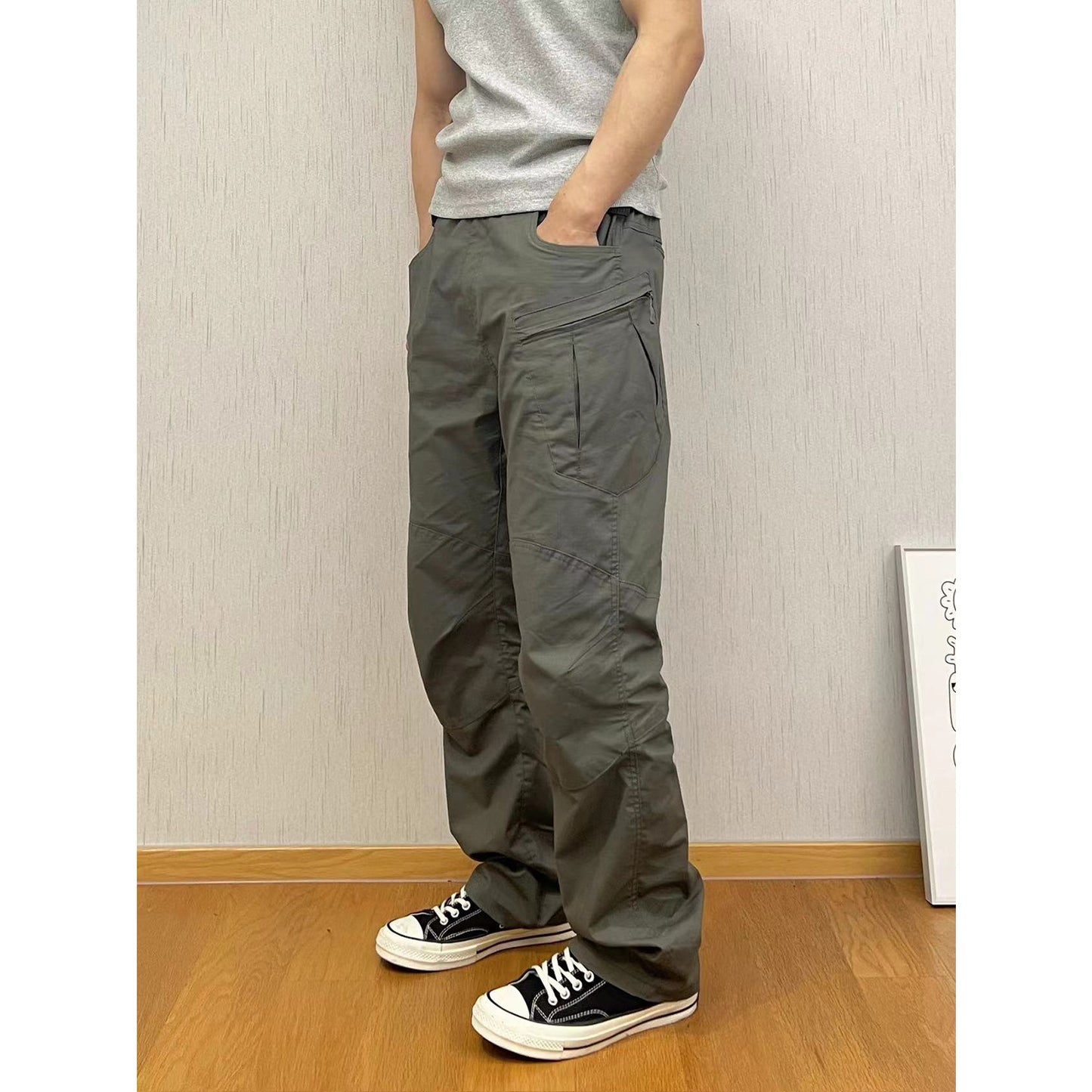 Person wearing gray pants and black sneakers standing against a plain wall.