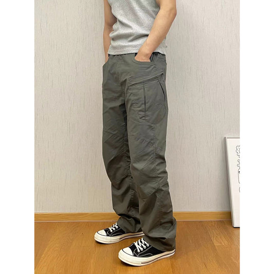 Person wearing gray pants and black sneakers standing against a plain wall.