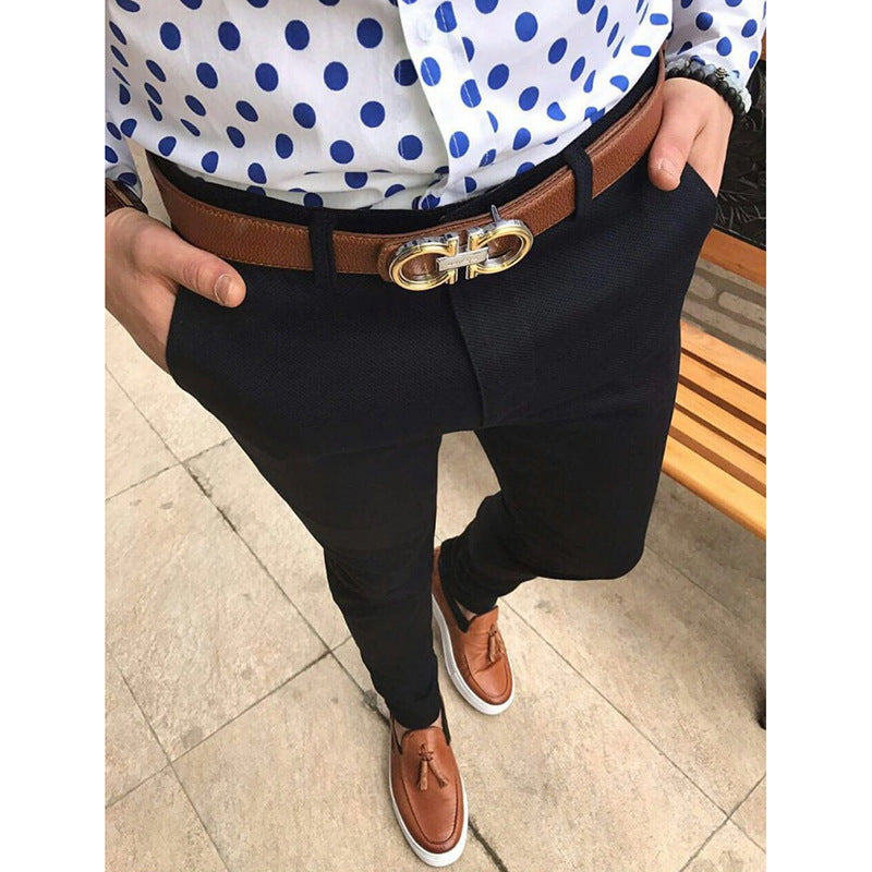 Person wearing a polka dot shirt, black pants, and brown shoes on a tiled floor.