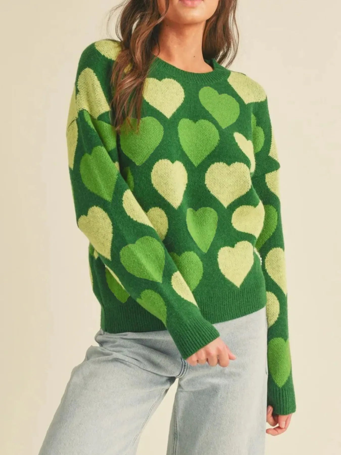 Person wearing a green sweater with heart patterns on a beige background