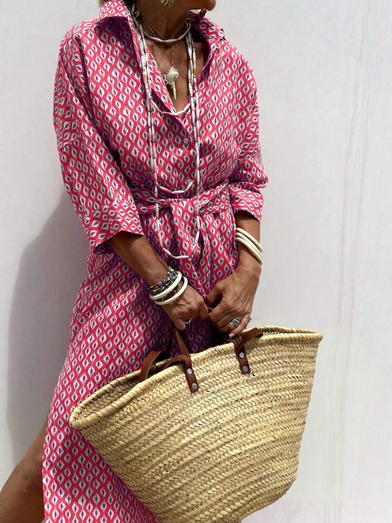 Person wearing a pink patterned dress holding a straw bag against a white background