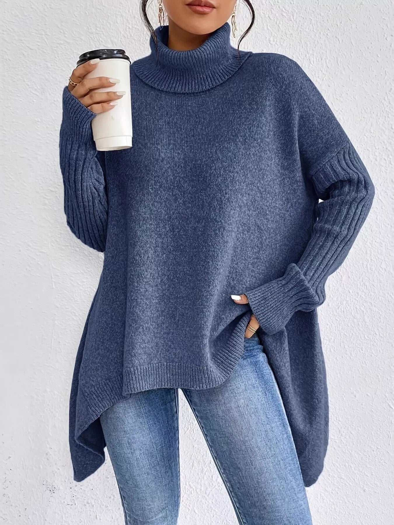 Person wearing a blue sweater and jeans holding a coffee cup against a white background