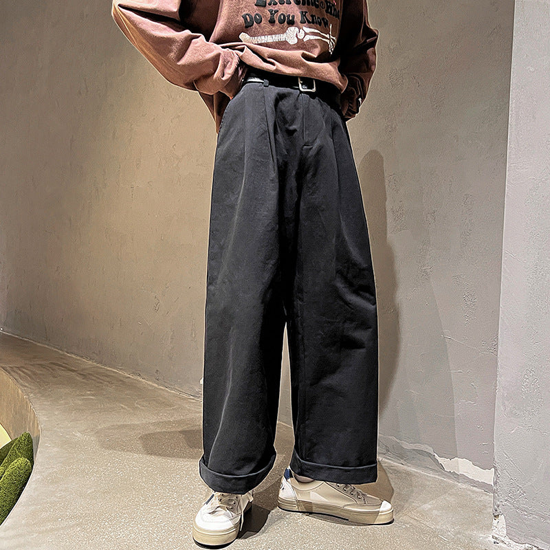 Person wearing a brown sweater and dark pants standing against a plain wall.