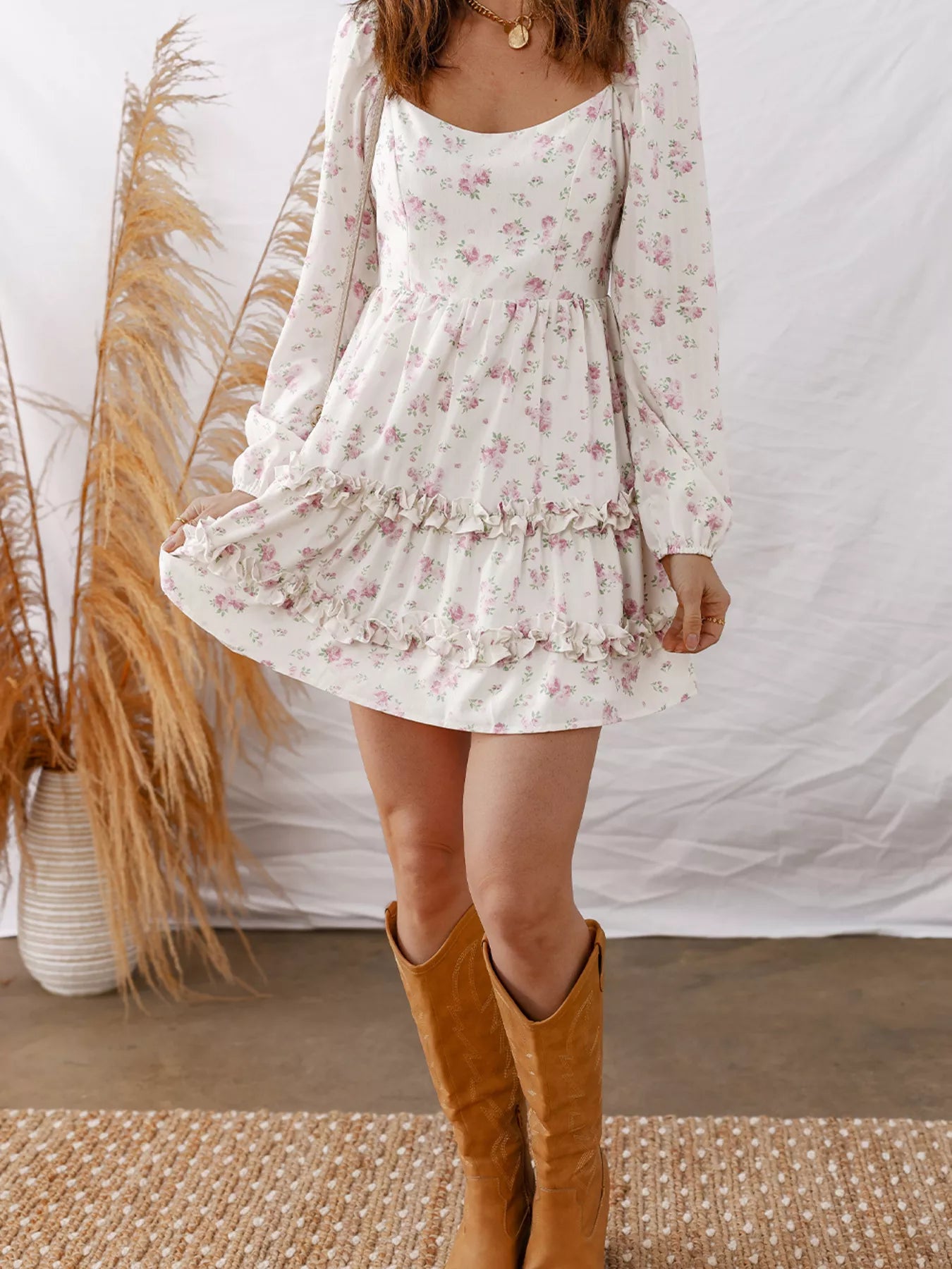 Person wearing a floral dress with long sleeves and brown knee-high boots, standing against a white backdrop.