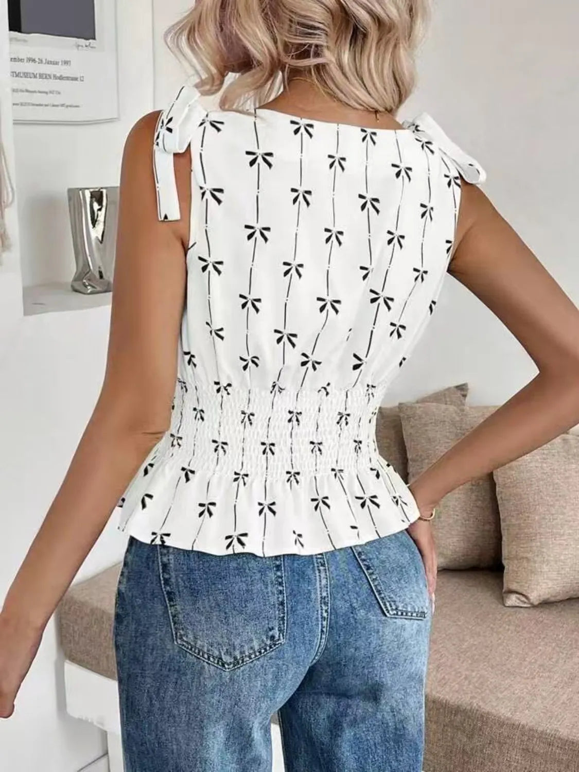 Woman wearing a white blouse with black bow patterns and blue jeans in a living room setting.