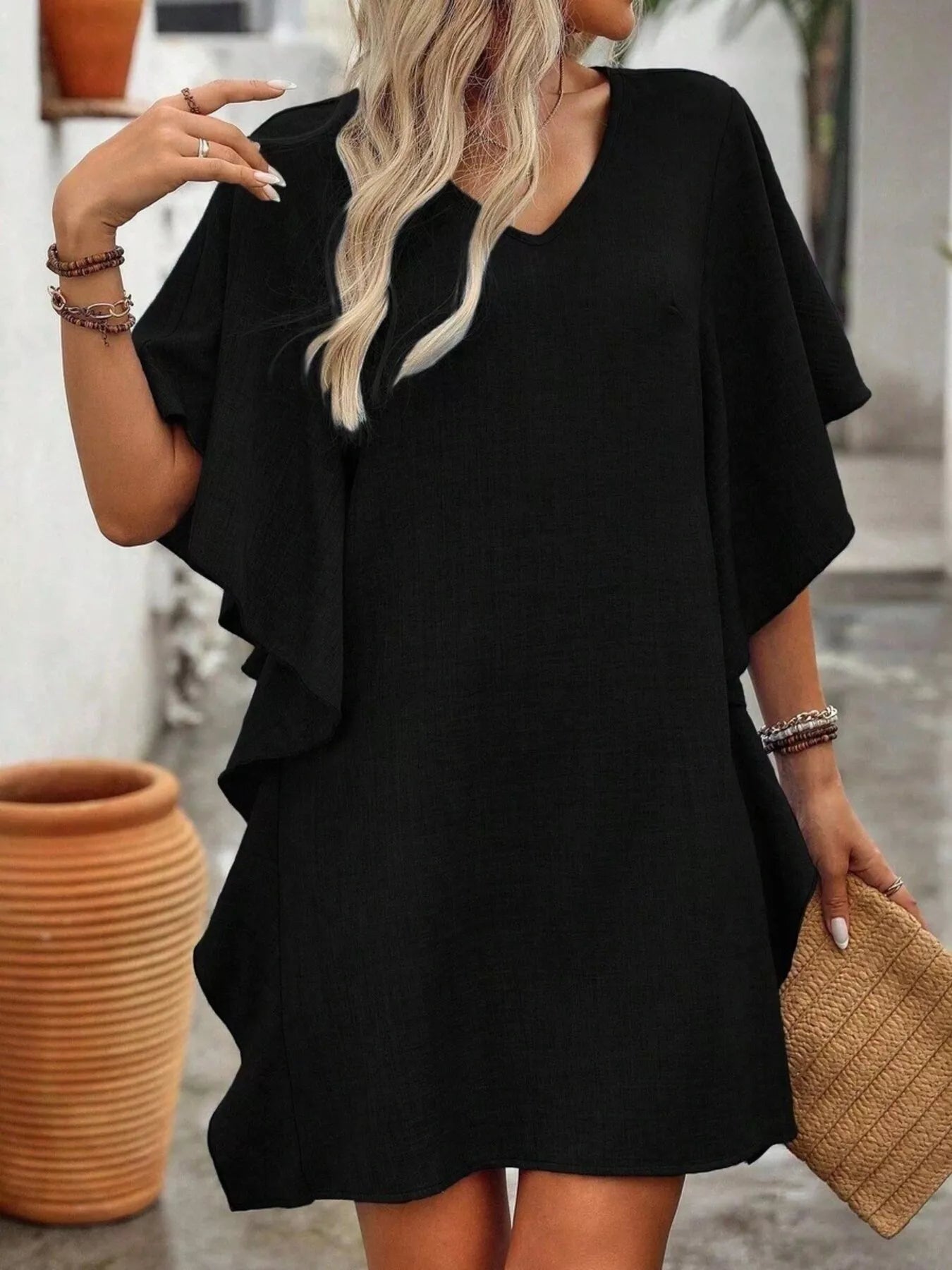 Woman wearing a black dress with ruffled sleeves, holding a woven bag.