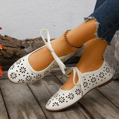 White floral-cutout flats worn by a person on a wooden floor.